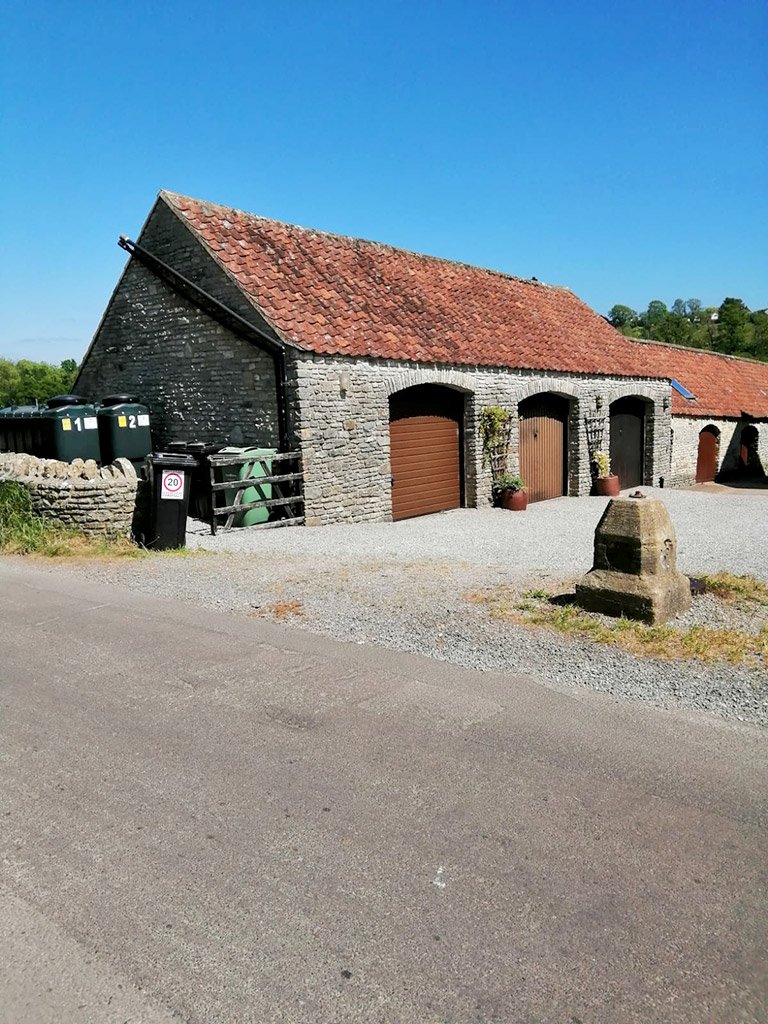 Stone barn with red tile roof, countryside setting.